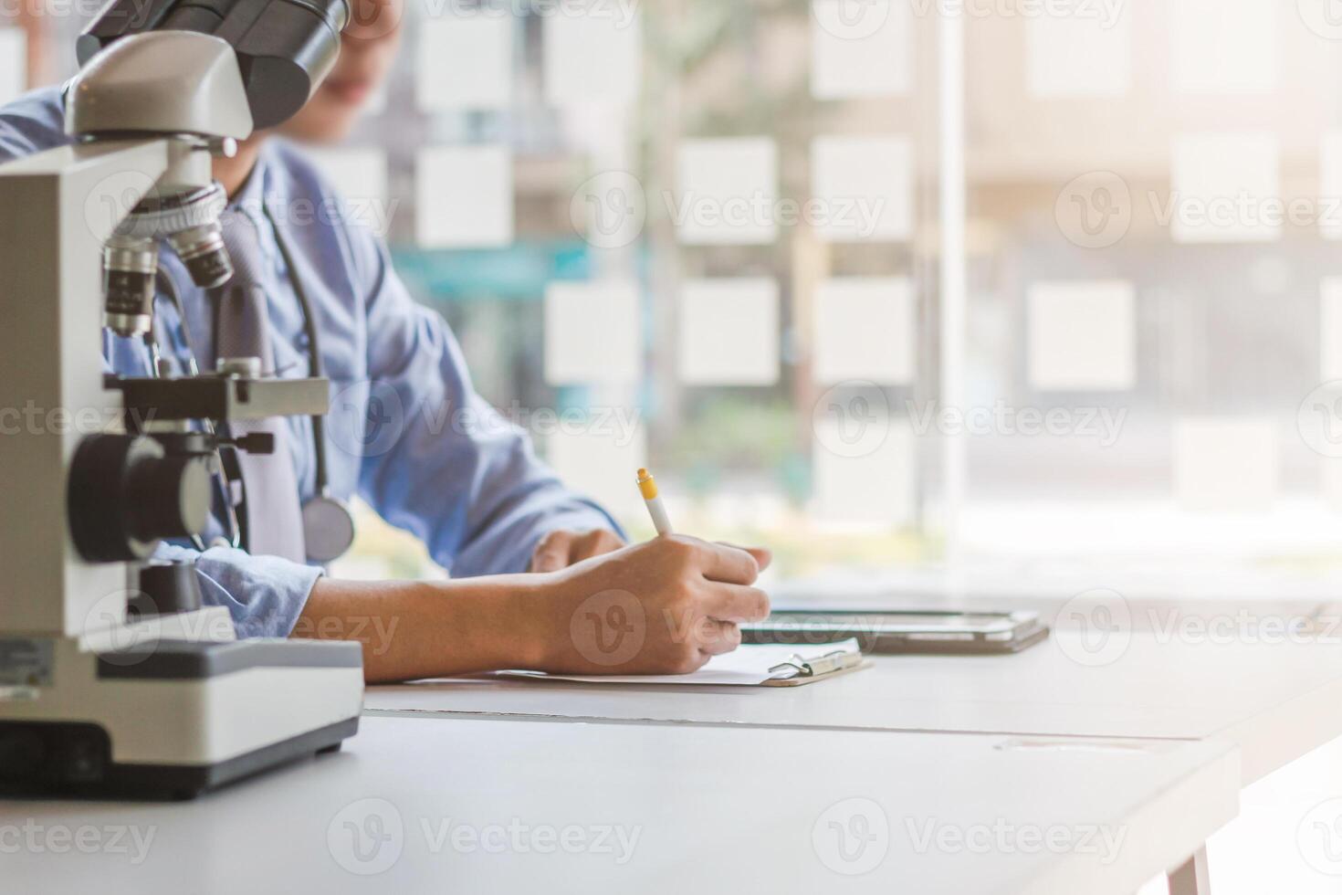 A man is writing on a piece of paper while sitting in front of a microscope photo