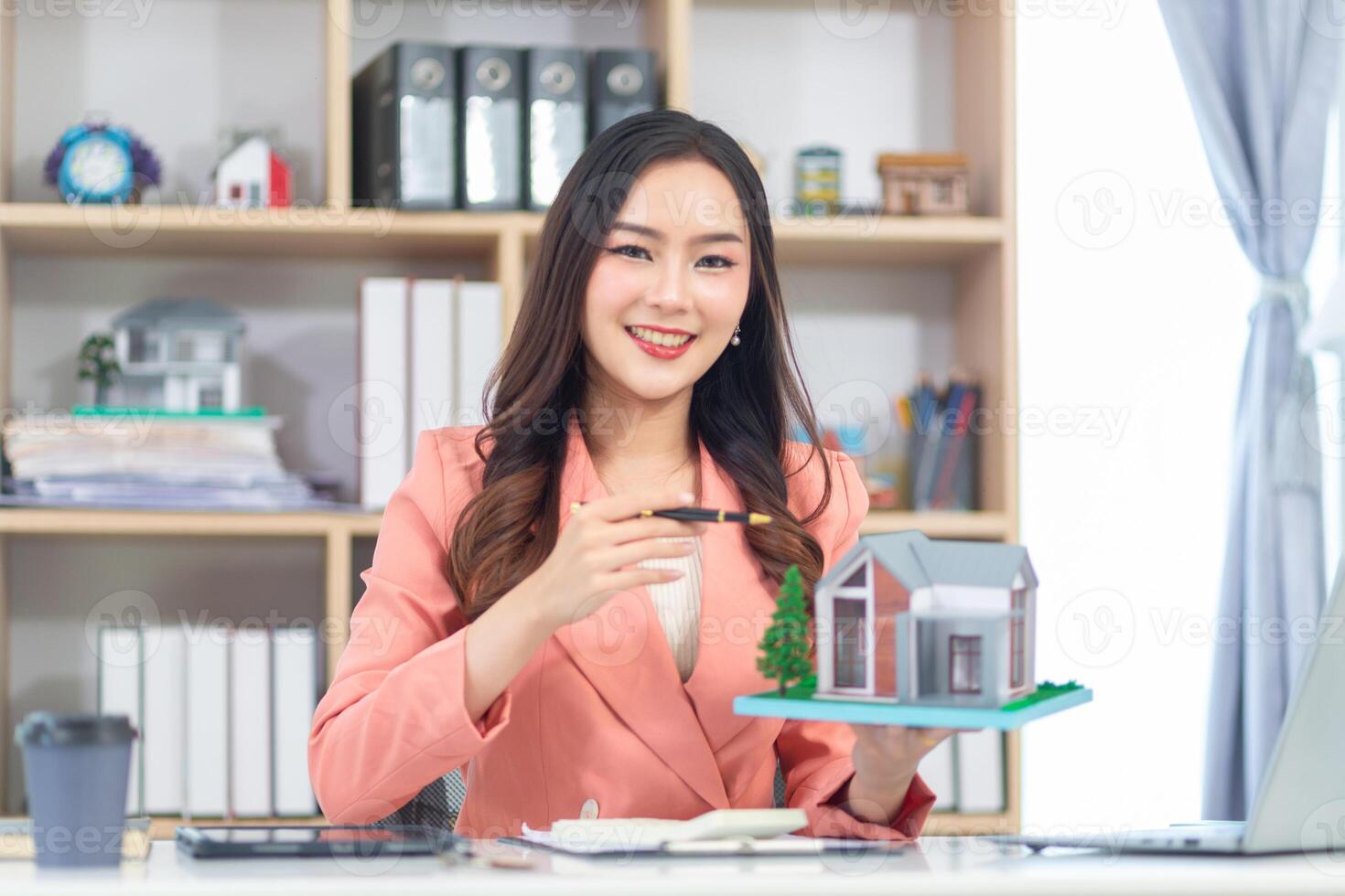 Asian woman holding a house model in front of her laptop photo
