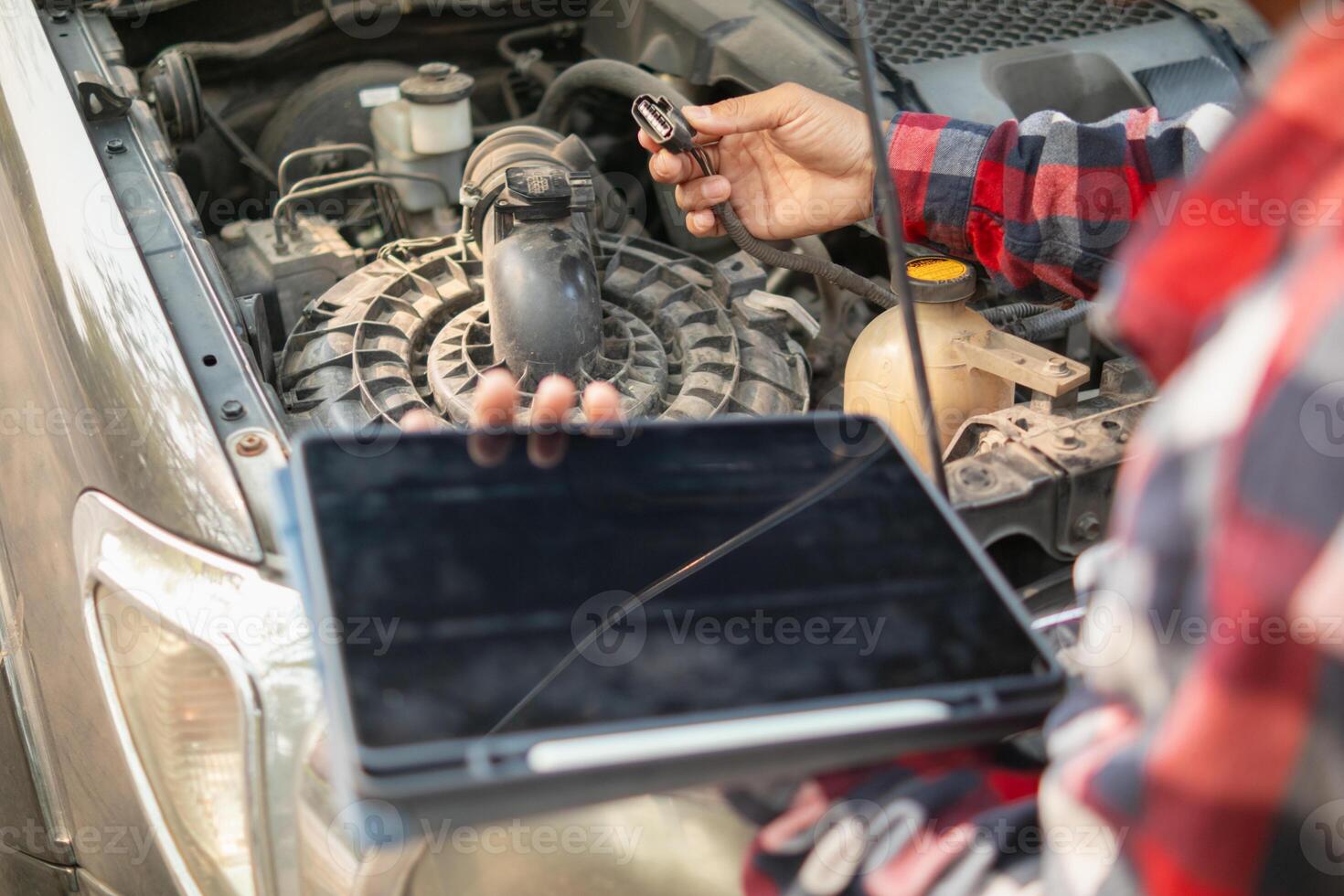 A man holding a tablet computer and looking at a car engine photo