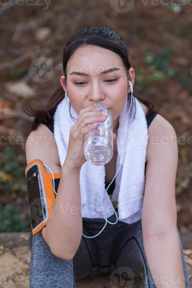 A woman is drinking water while sitting on a bench photo