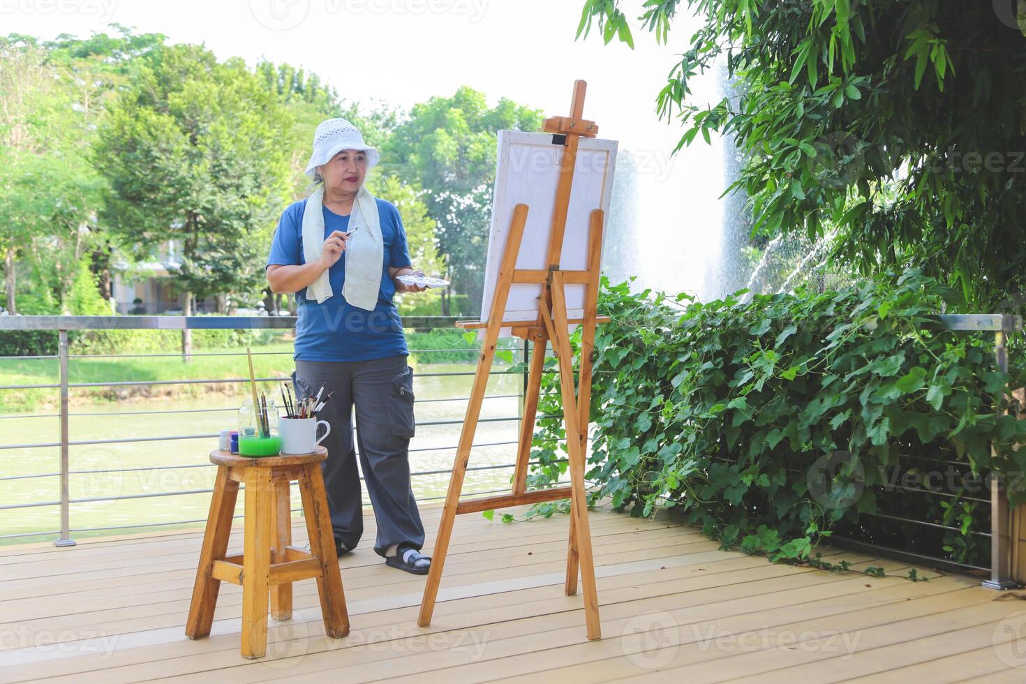 Artist Painting Outdoors by a Lake in Nature, Senior Woman Enjoying Plein Air Painting Session, Artist Capturing Scenery on Canvas photo