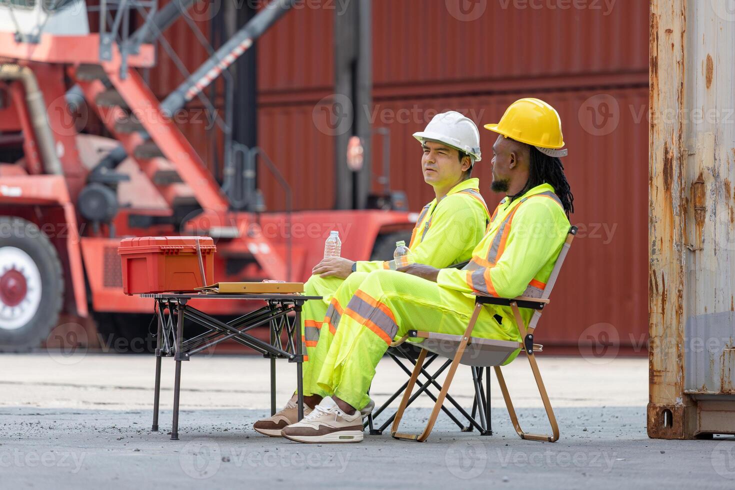 Two Construction Workers on Break at Industrial Site, Diverse Male Laborers Resting Outdoors with Safety Gear, Workers Taking a Lunch Break at Industrial Port photo