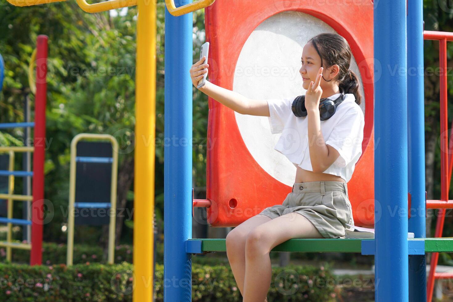 Young Asian Girl Taking a Selfie at a Colorful Playground, Child Posing for a Photo on Her Smartphone in a Park, Happy Kid Enjoying Technology and Outdoor Play