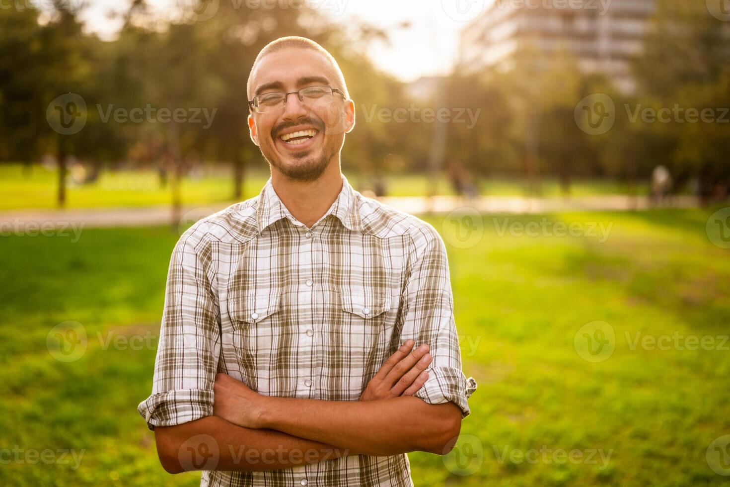 Portrait of a cheerful adult man smiling with arms crossed, enjoying a sunny day outdoors in a park. photo