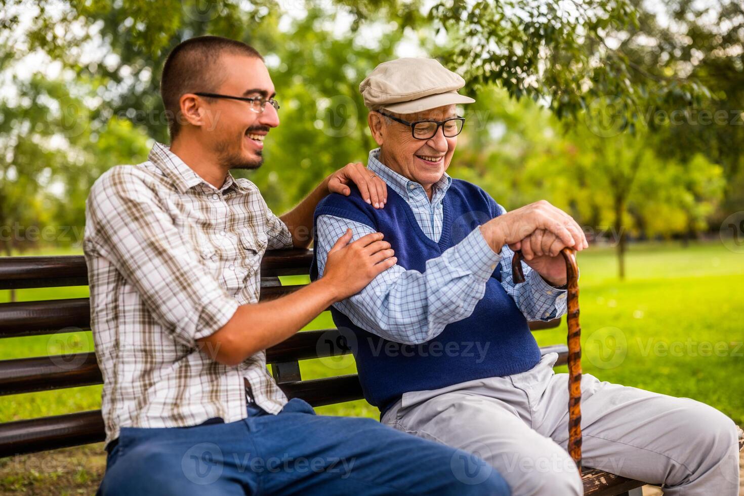 Grandfather and grandson sitting on a park bench, smiling and enjoying a warm sunny day together. photo