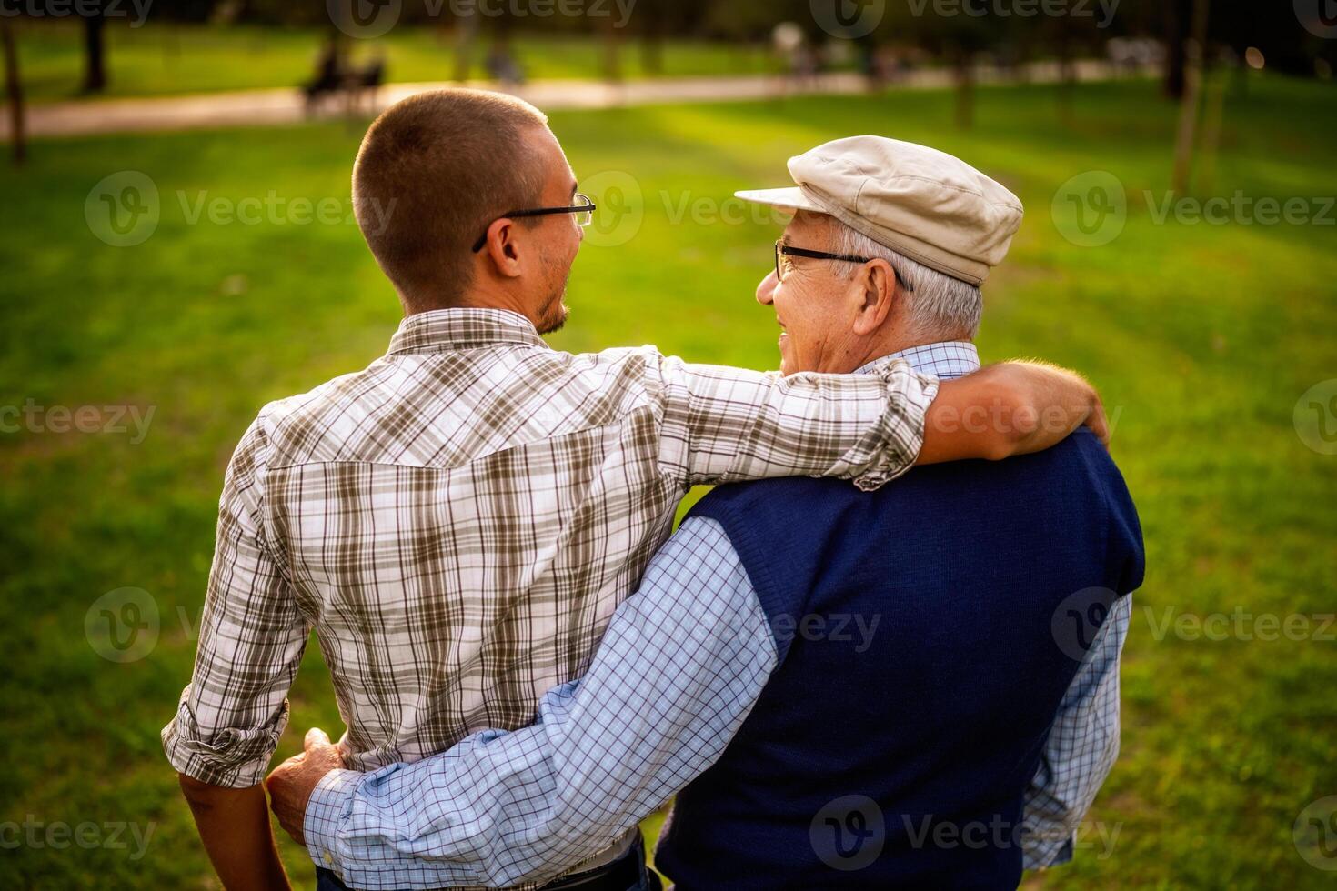 Caucasian grandfather and grandson hugging each other tightly in a park, reflecting real moments of family love. photo