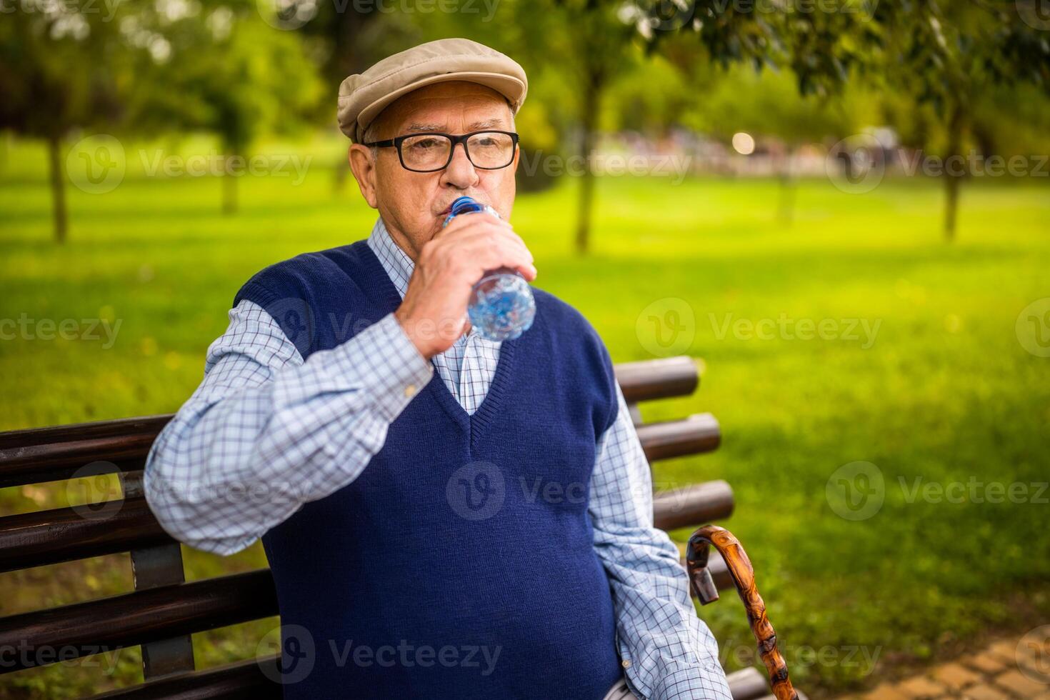 Active senior male relaxing in casual sweater and hat, drinking water for hydration and vitality during a sunny day walk. photo
