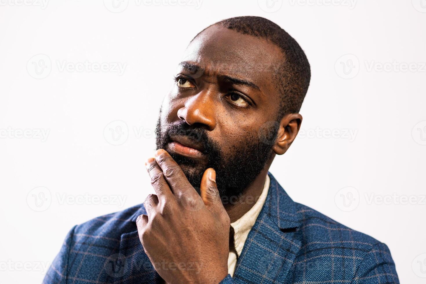 Close up portrait of a confident African American businessman in a suit, deep in thoughtful contemplation with hand on chin against a gray background. photo