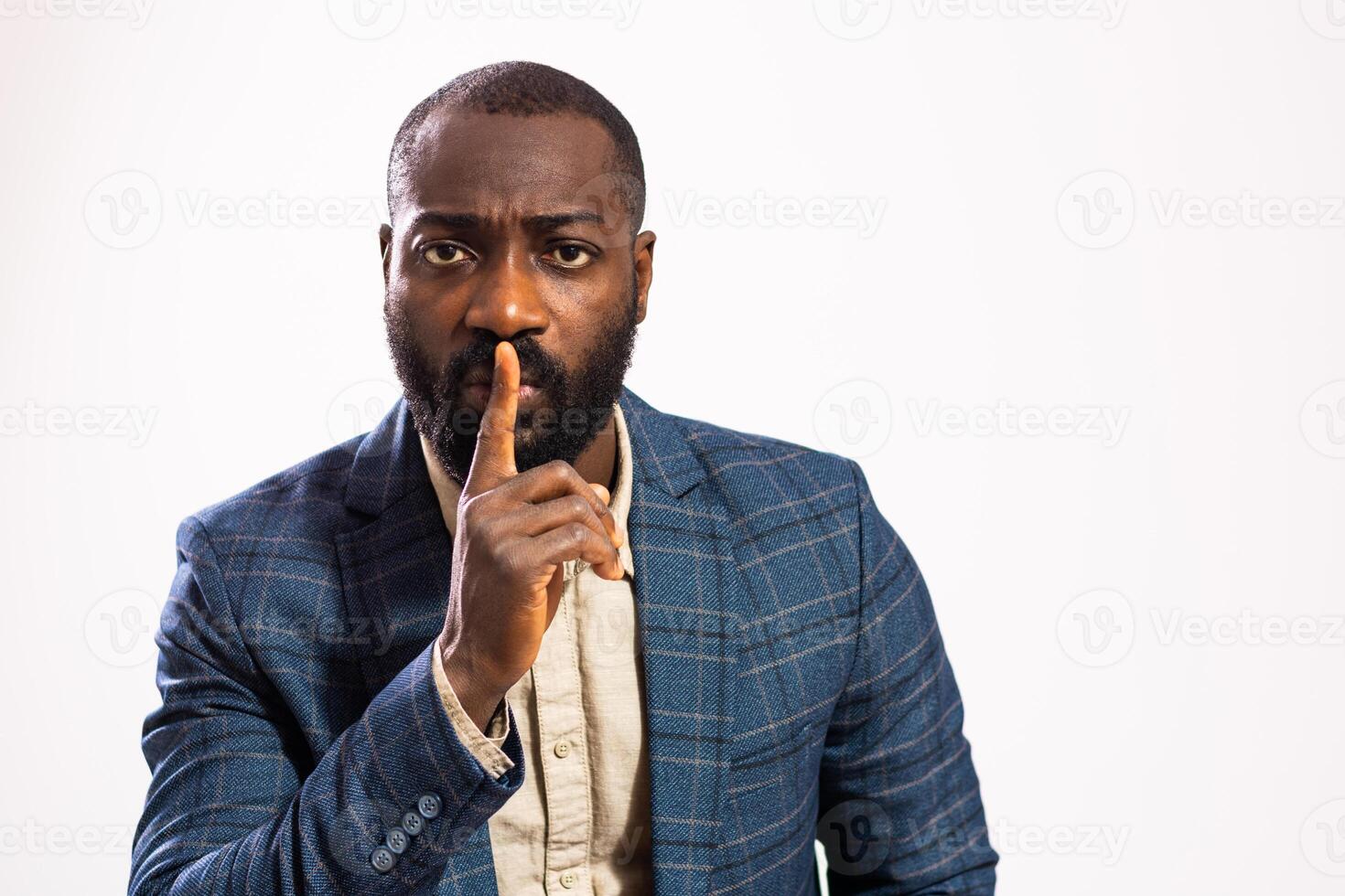 Studio portrait of African ethnicity male in business suit with finger on lips, conveying serious message of silence and focus. photo