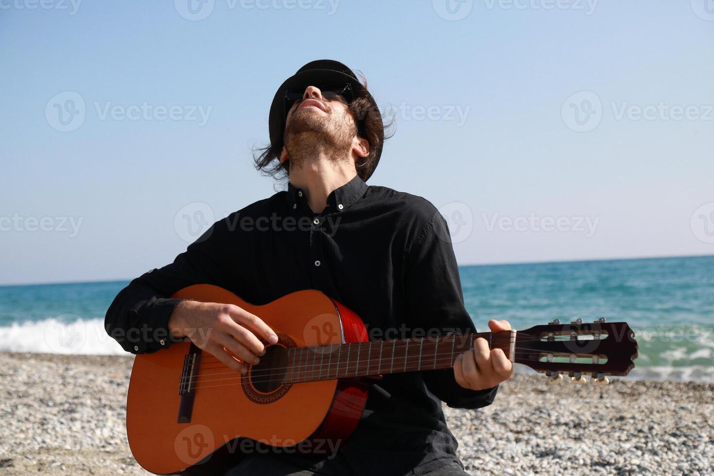 Kneeling Man Plays Guitar Musical Instrument On The Beach Near The Ocean Summer Outdoor photo