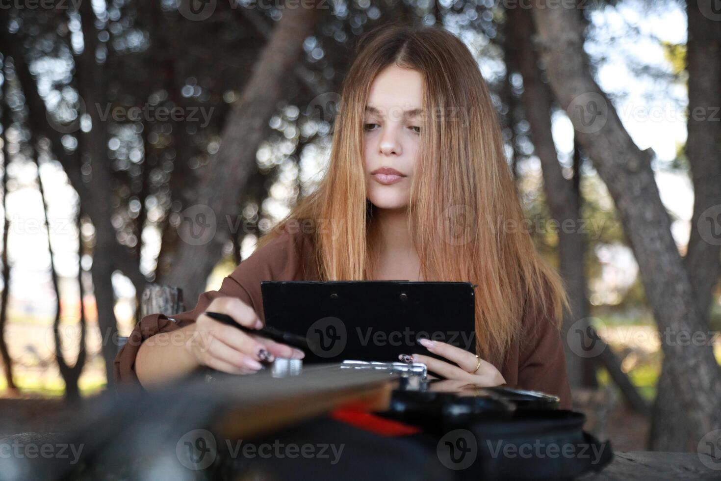 Girl Writes Music Notes On Sheet Music At The Park Table In The Nature photo