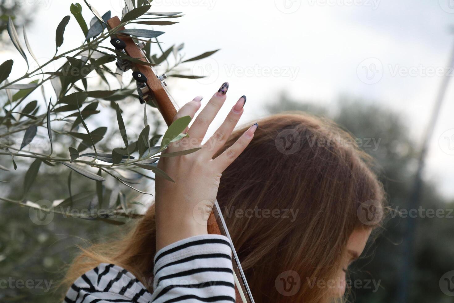 Artist Girl Plays Ukulele Musical Instrument Outside In Park Near A Tree Outdoor photo