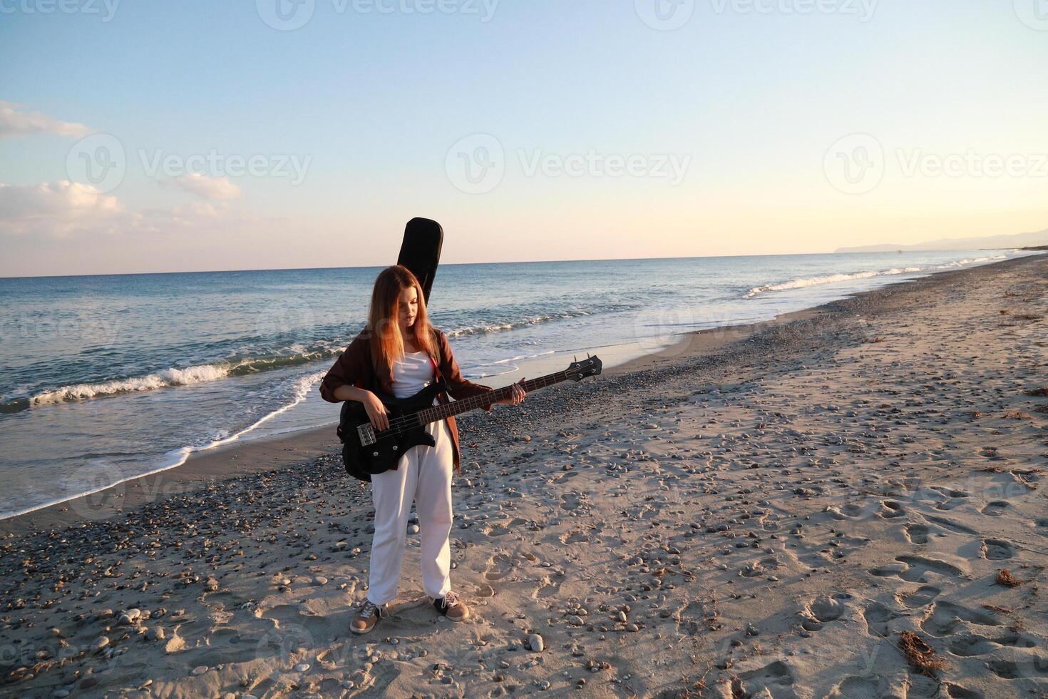 Girl Walks And Plays The Bass Instrument On The Beach Near The Sea At Sunset photo