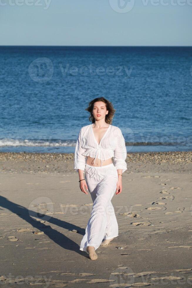 Italian Short Hair Girl Dances On The Soft Beach Near Ocean In White Clothes photo