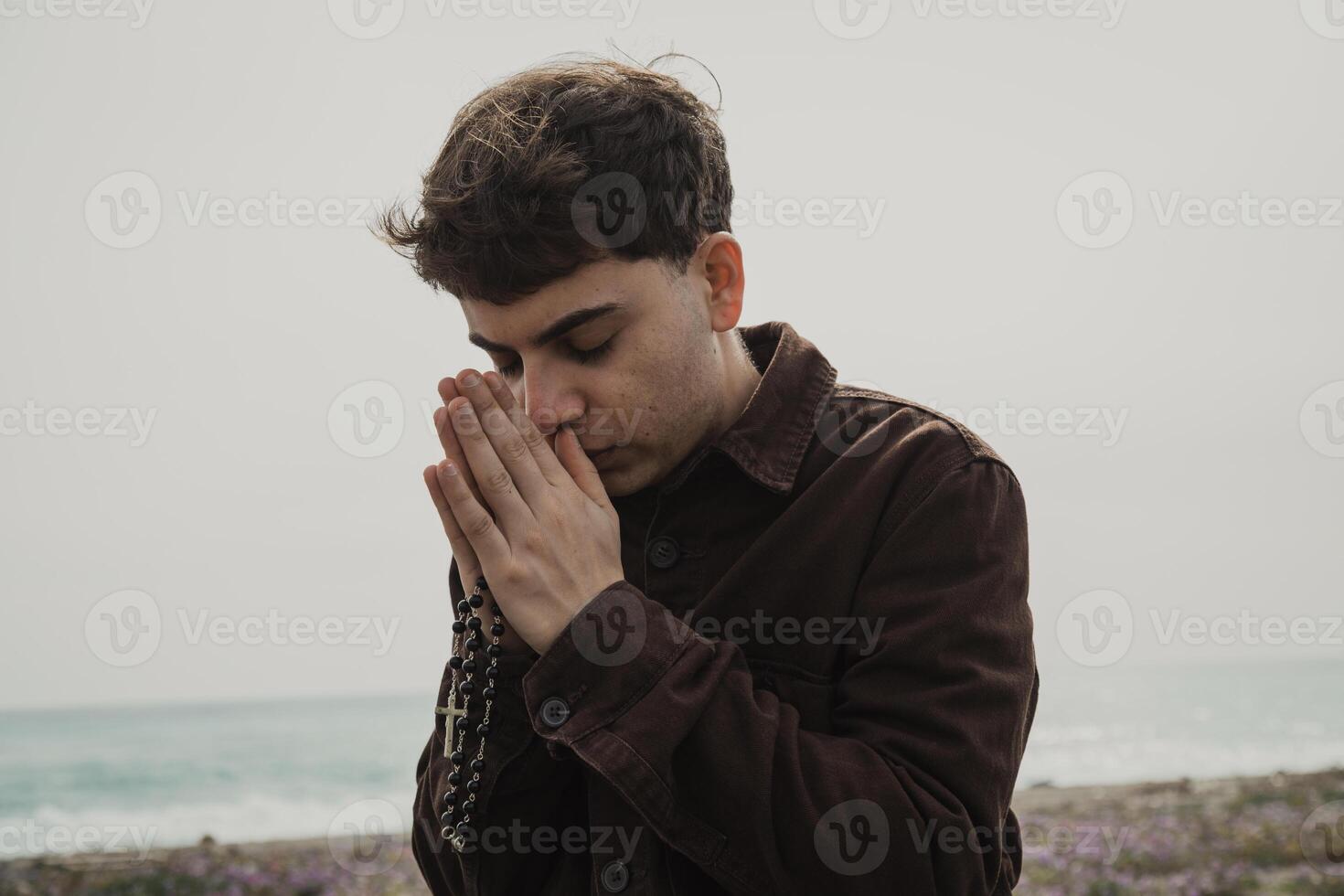Boy Praying With A Rosary And Eyes Closed On The Shore photo