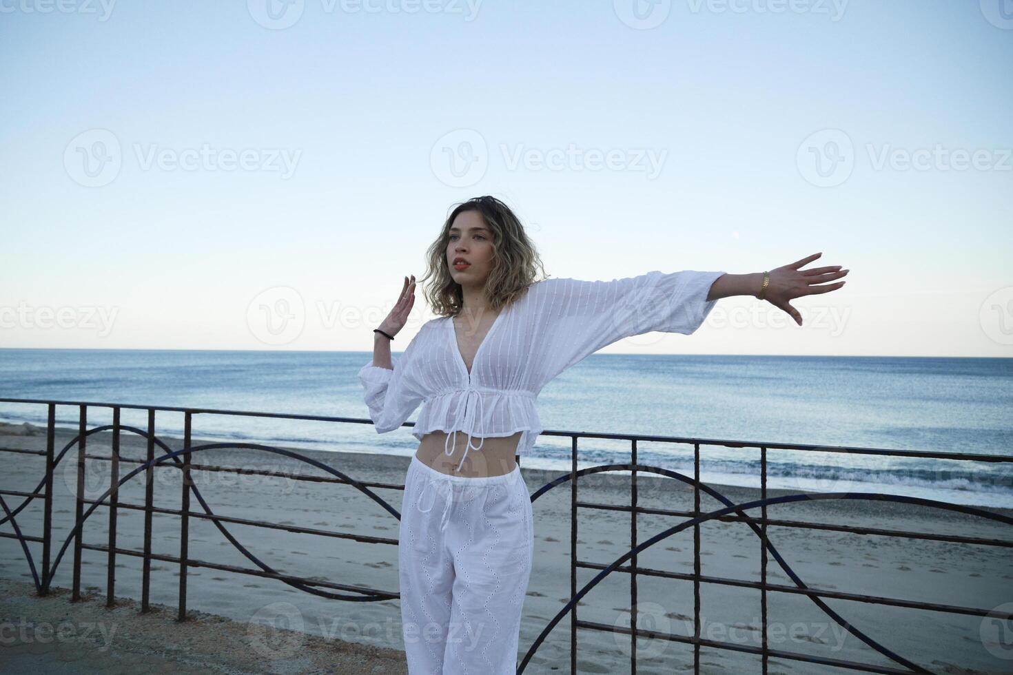Girl in White Clothing Dances Along Seaside Pavement photo