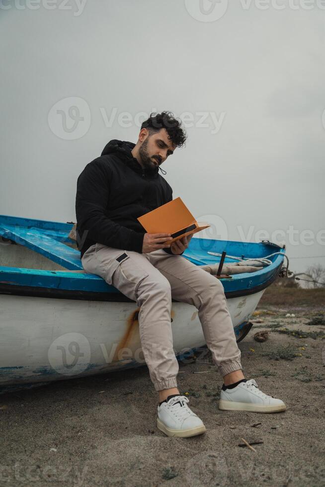 Man Carefully Reads A Book While Relaxing By The Sea In Winter photo