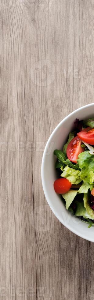 Fresh salad in a white bowl on wood grain surface with vertical negative space above for text photo