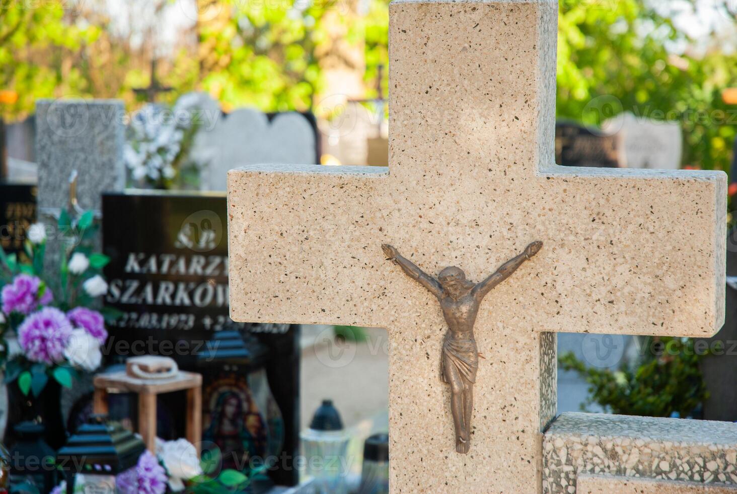 Ornate stone cross with jesus christ figure in peaceful sunlit cemetery with colorful flowers and monuments in serene background photo