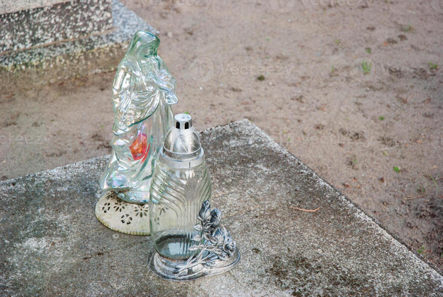 Weathered concrete base with illuminated glass mary statue and ornate candle holder in serene outdoor cemetery setting photo