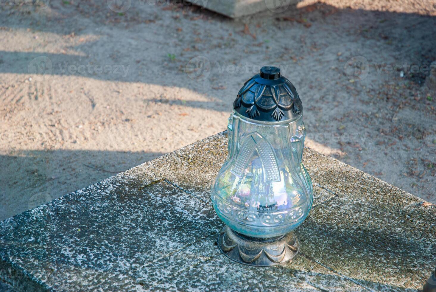 Elegant glass candle lantern with intricate design on stone surface in sunlit outdoor cemetery setting creates a serene and reflective atmosphere photo