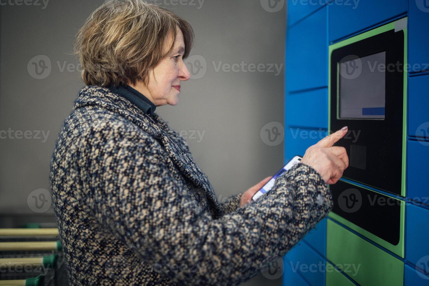 elderly woman taps the display to receive a parcel. A mature lady in casual clothes photo