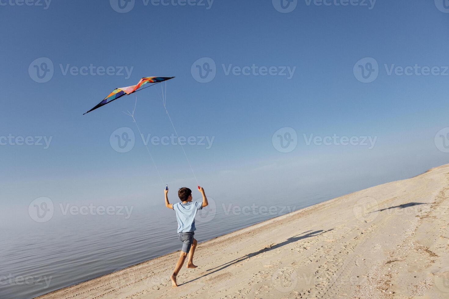 A little boy flies a kite on the seashore. The child is running along the sandy beach and having fun outdoors. A child plays by the ocean on summer vacation. photo