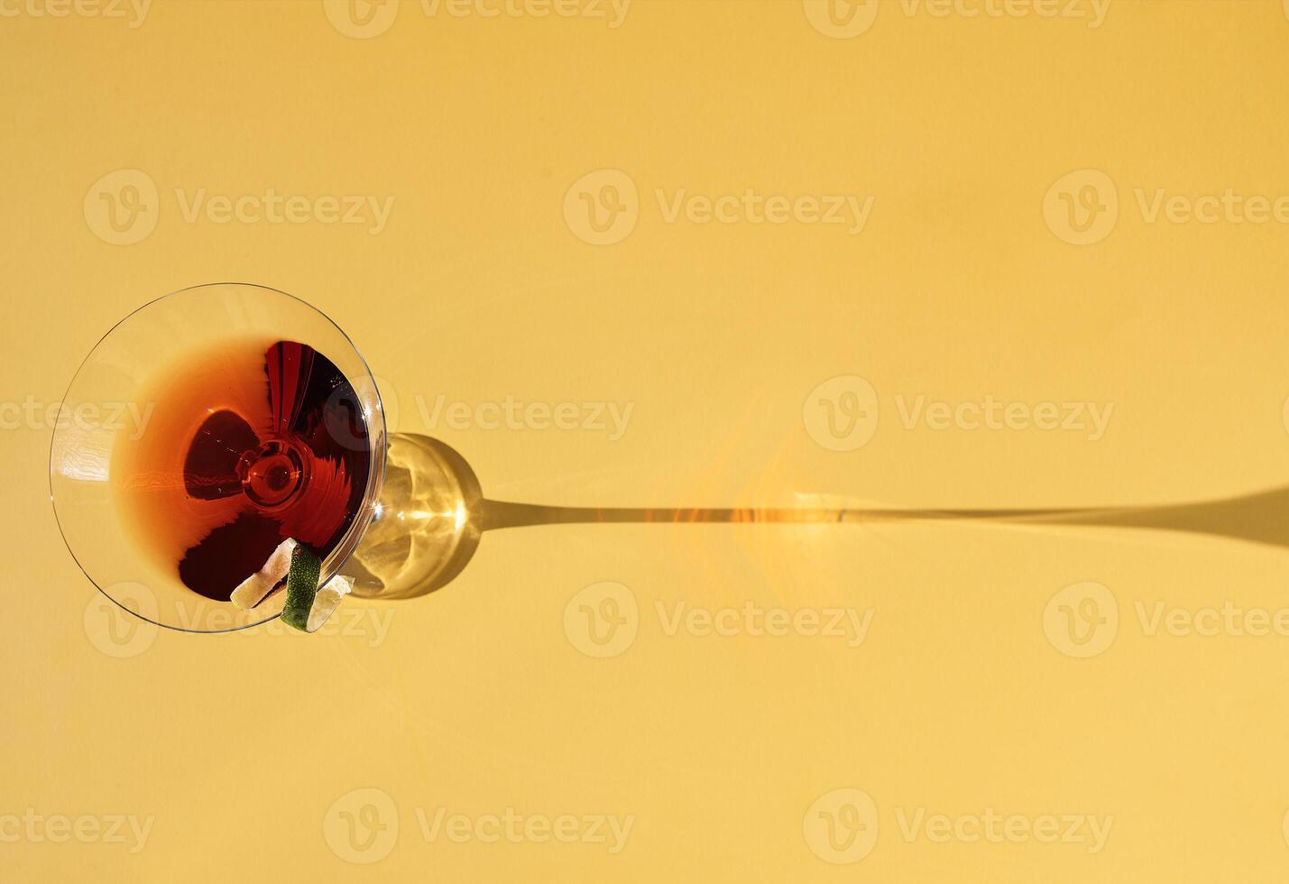 Close-up of a martini glass on a yellow background. View from above. An elegant goblet with a red alcoholic sparkling drink decorated with lime zest. Sunlight. photo