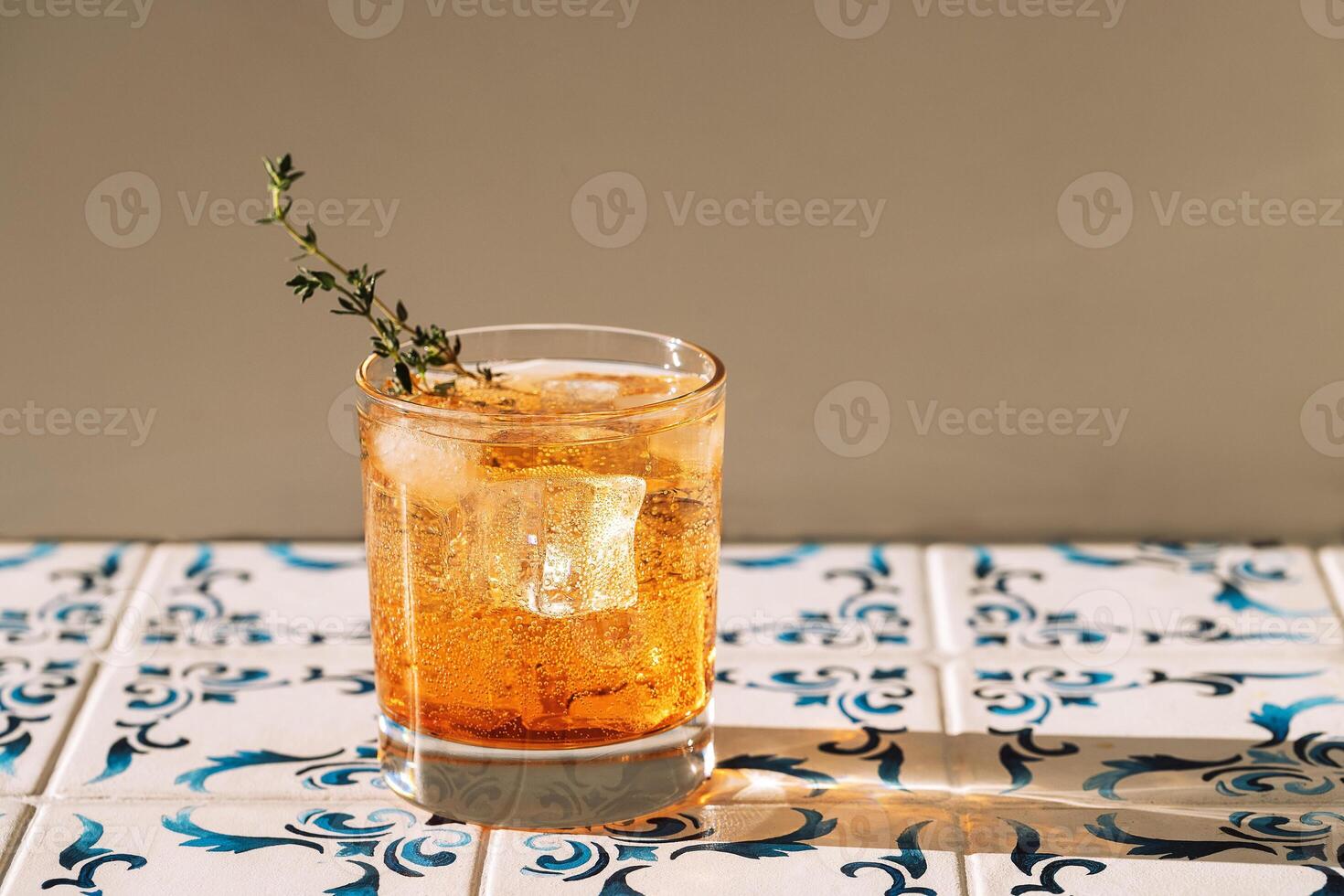 Close-up of a glass of soda and ice cubes with a sprig of thyme. Cool and delicious mineral water with fresh leaves. A sweet carbonated drink on a table with patterned tiles. photo