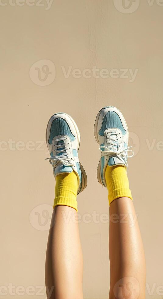 Stylish legs in vibrant yellow socks and trendy blue sneakers are raised against a soft beige background, showcasing a playful and energetic fashion statement with a modern aesthetic photo