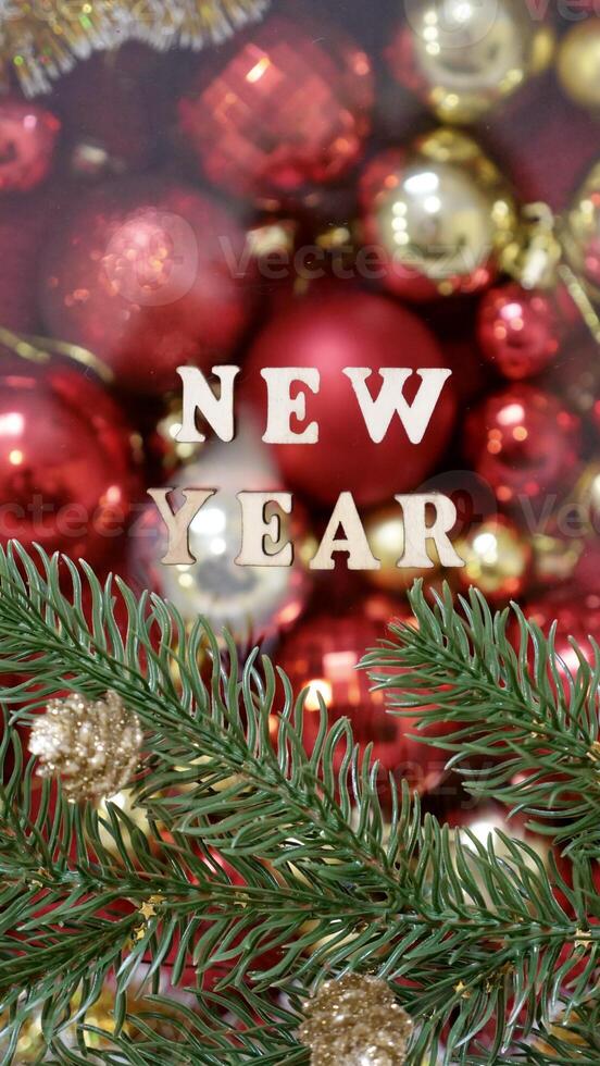 Christmas flatley with New Year lettering on blurred red gold background baubles decoration. Close-up, shiny composition. Postcard . Vertical photo