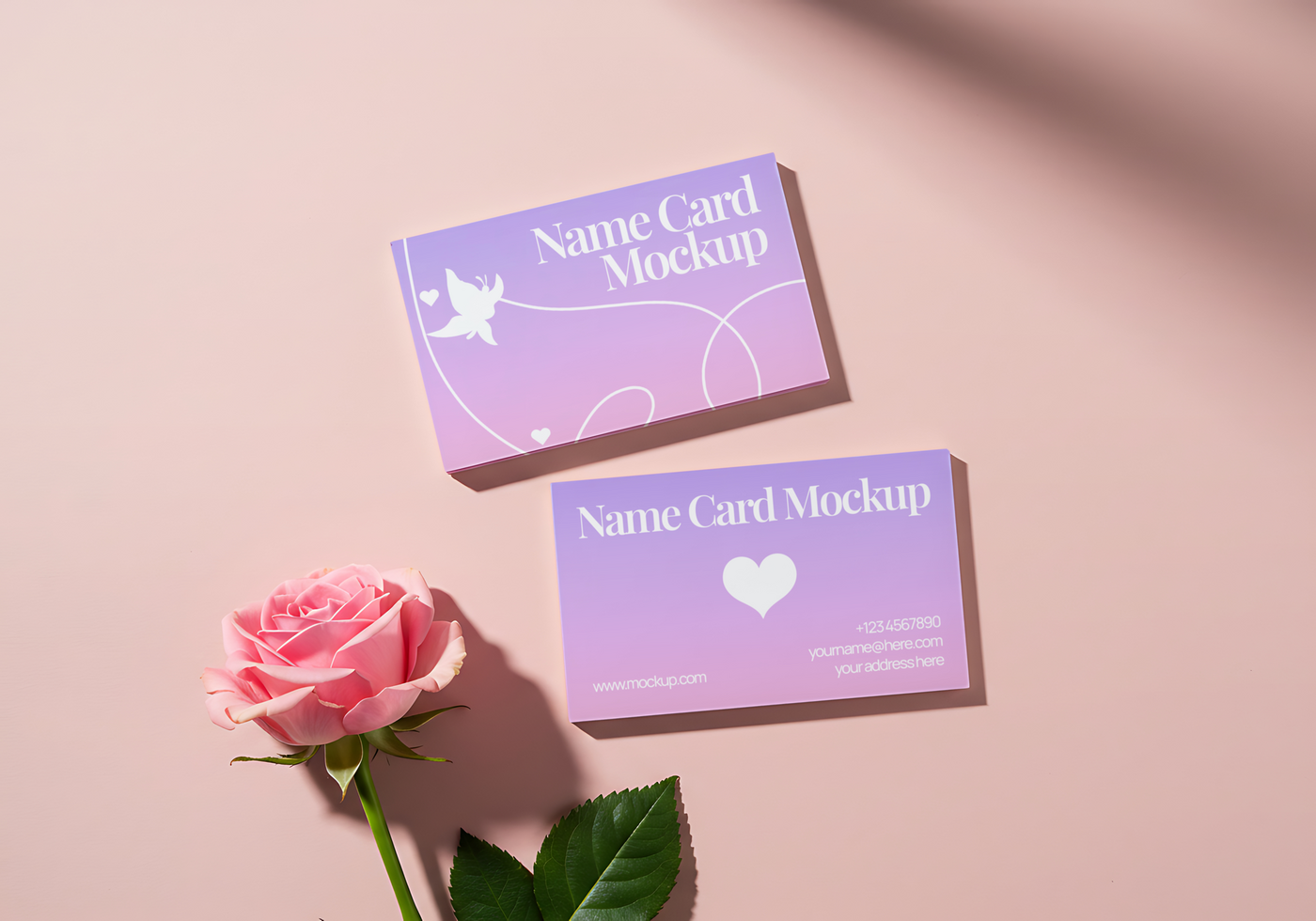 Two pastel purple name card mockups lie beside a pink rose on a pink background psd