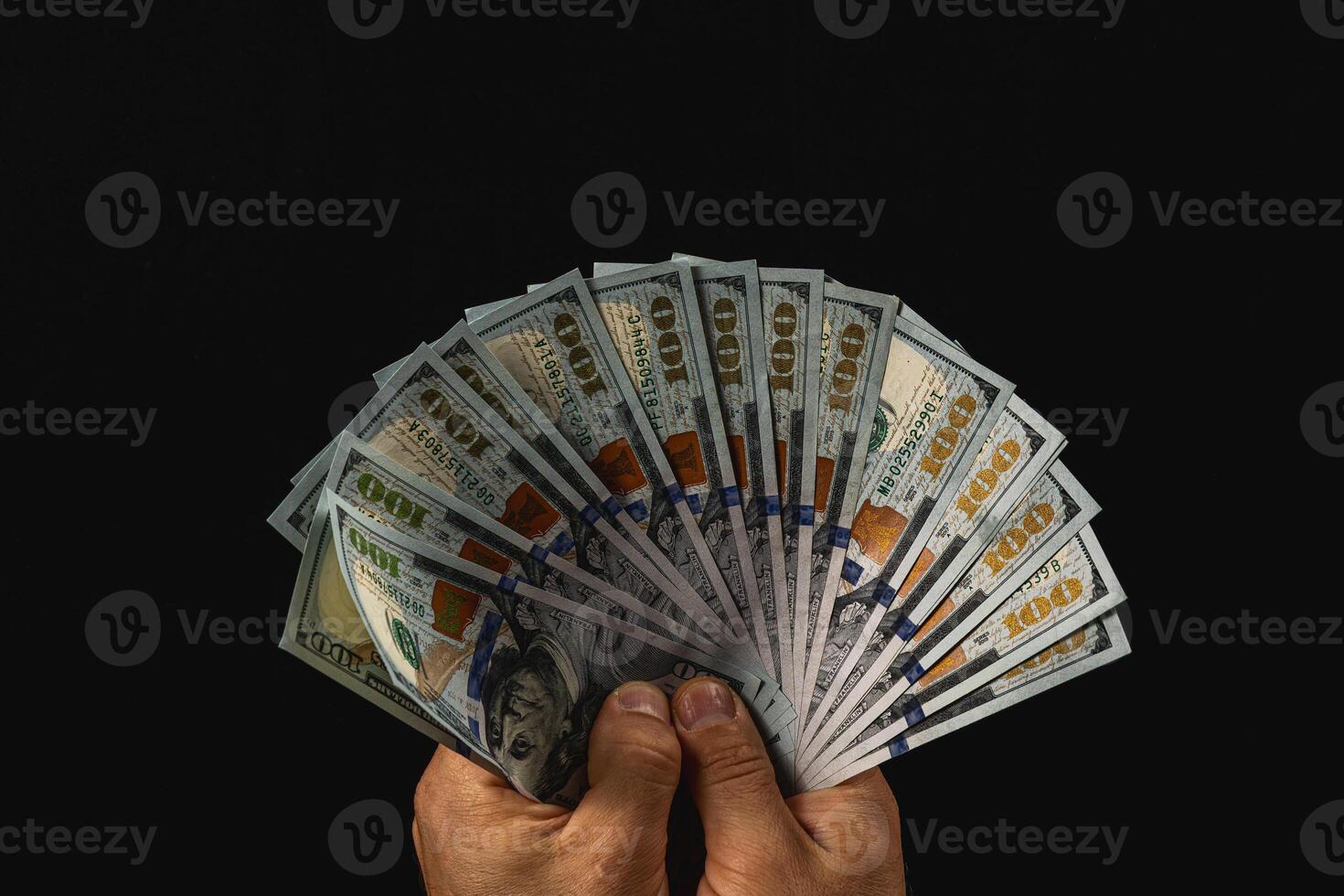 Hands show a fan of hundred-dollar bills on black photo