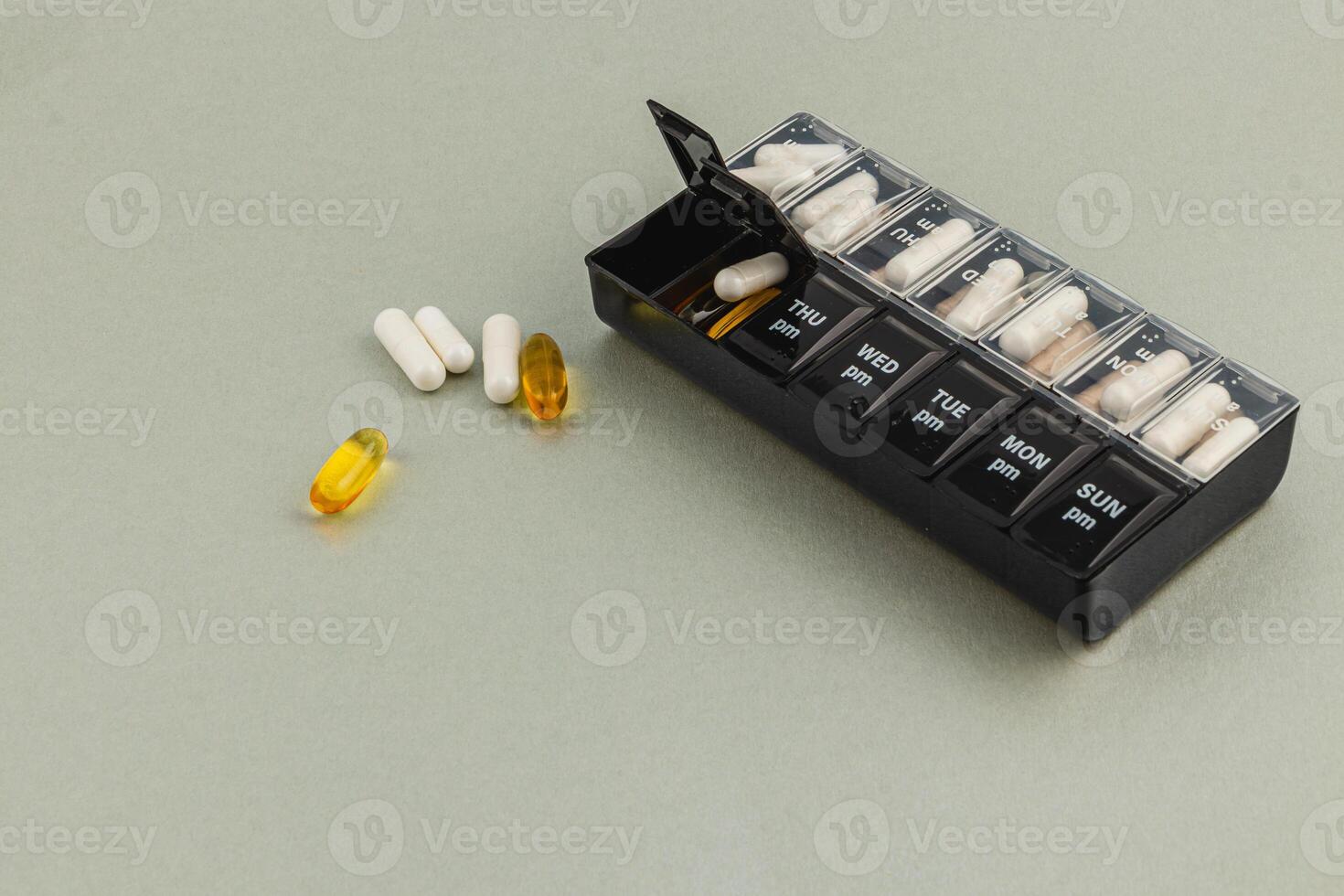 Weekly pill organizer with various medications on a gray surface photo