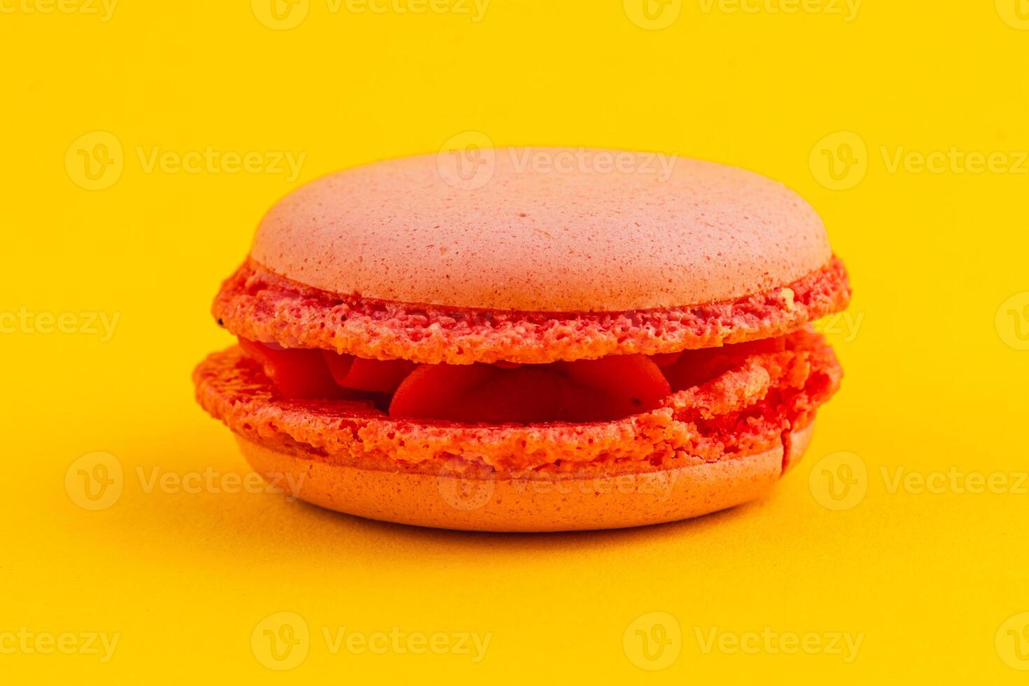 Bright orange macaron on vibrant yellow background photo