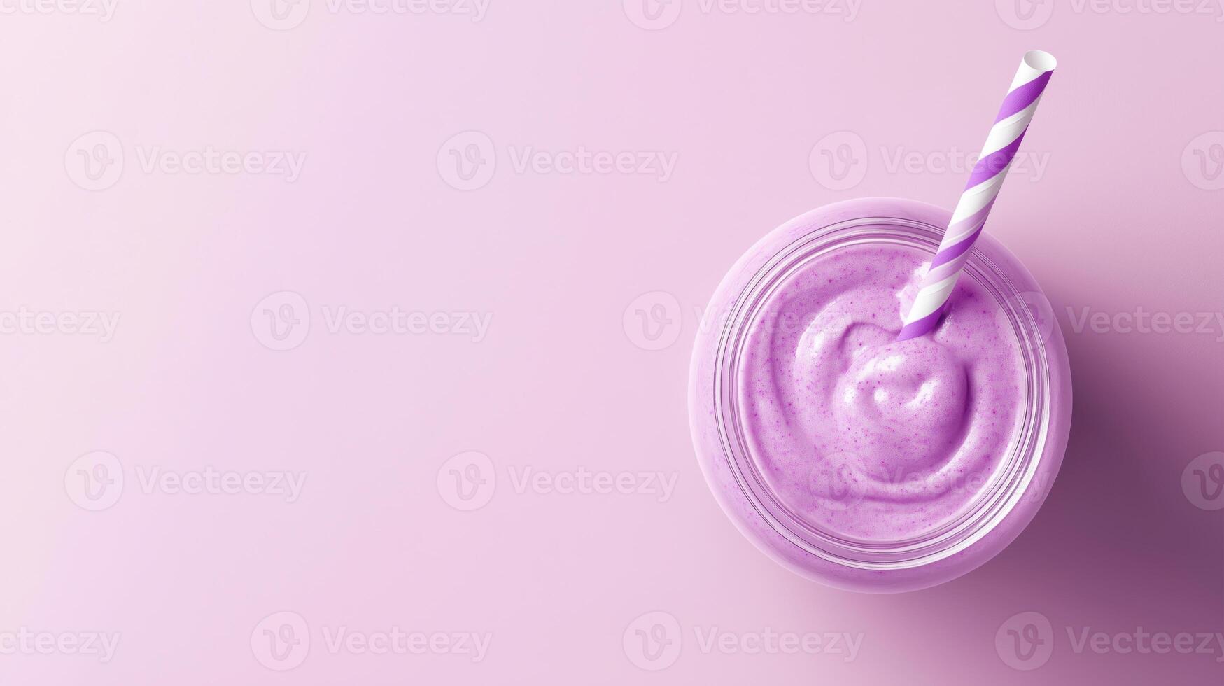 glass jar with a violet and white striped straw. The jar is filled with a purple smoothie or milkshake. The background is a light purple color. photo