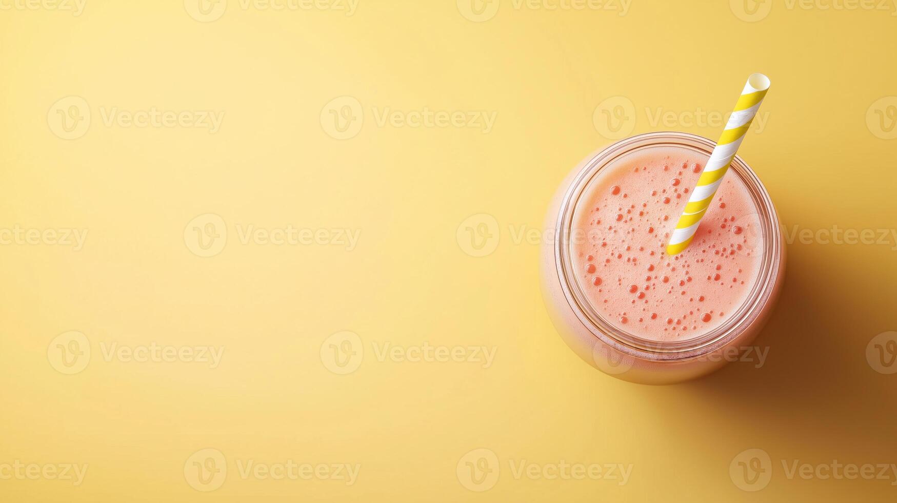glass jar with a yellow and white striped straw. The jar is filled with a orange smoothie or milkshake. The background is a light yellow color photo