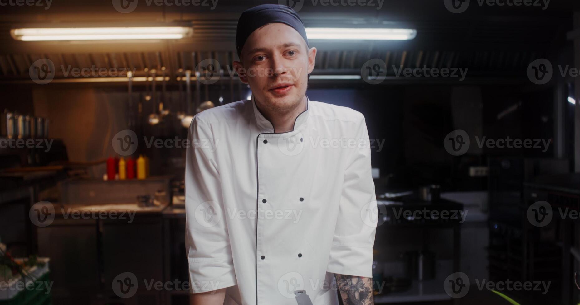 A man in a chef's uniform speaks and shows the products standing near the frying pan in the kitchen of the restaurant photo