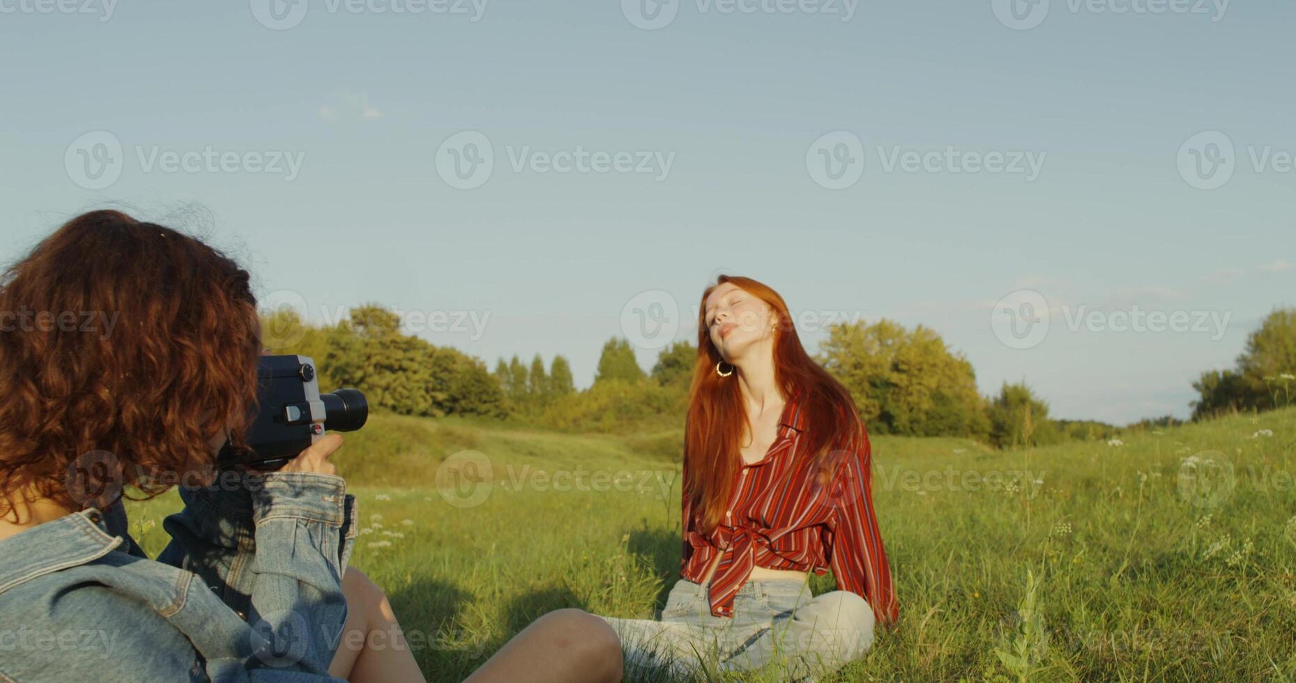 Two young women are photographed with a camera in the grass in a field. A sunny summer day photo