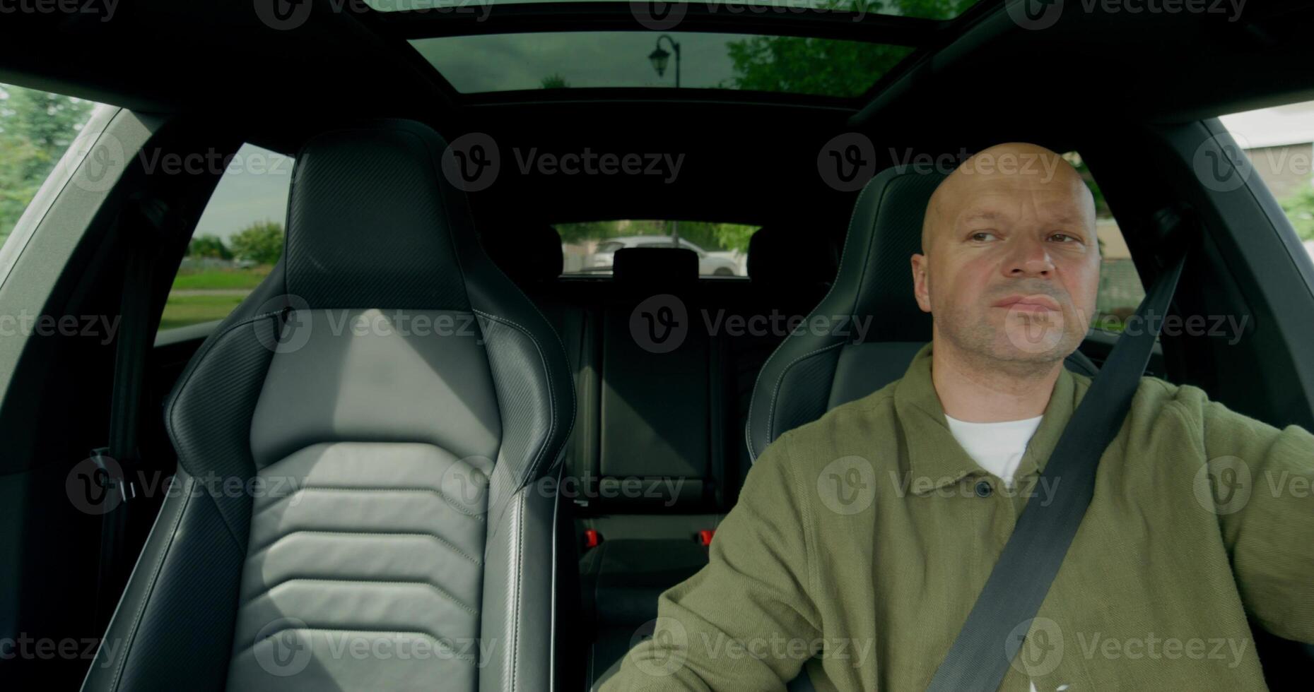 The man is driving the car, he is wearing a seat belt. Front view photo