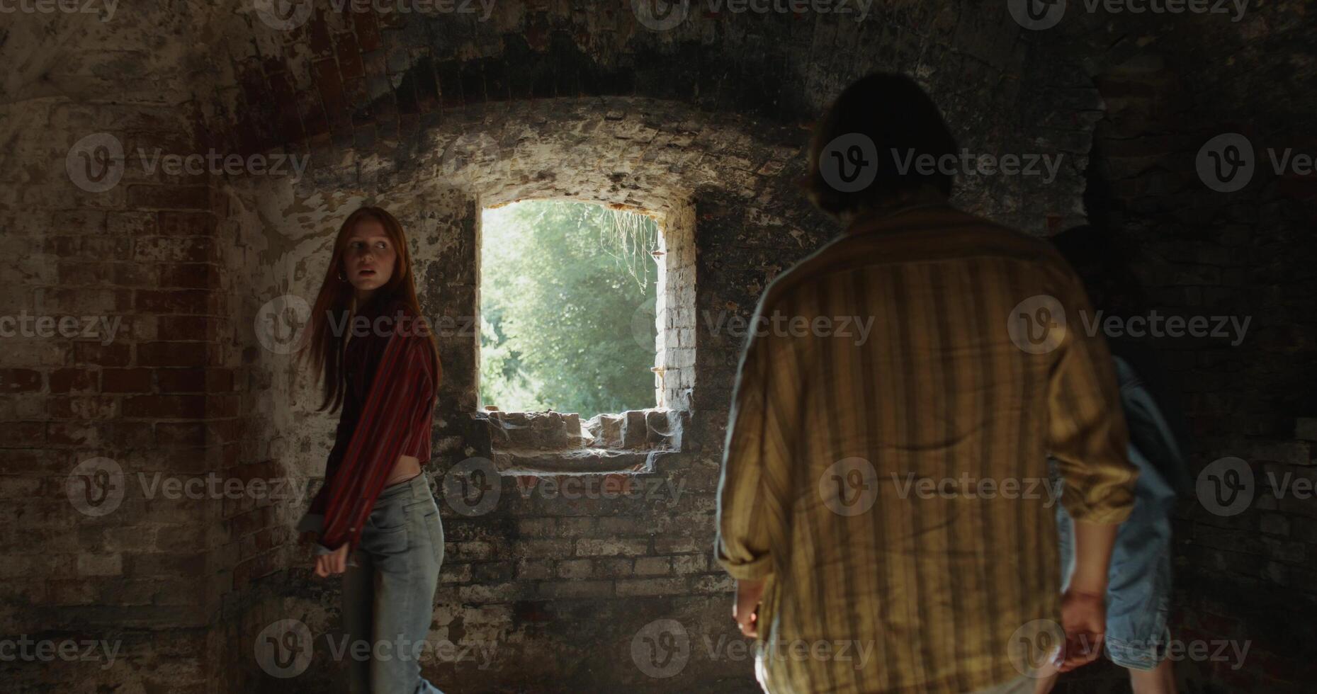 friends smile and talk as they walk around a room in a historic abandoned brick building. Sunlight in the window photo