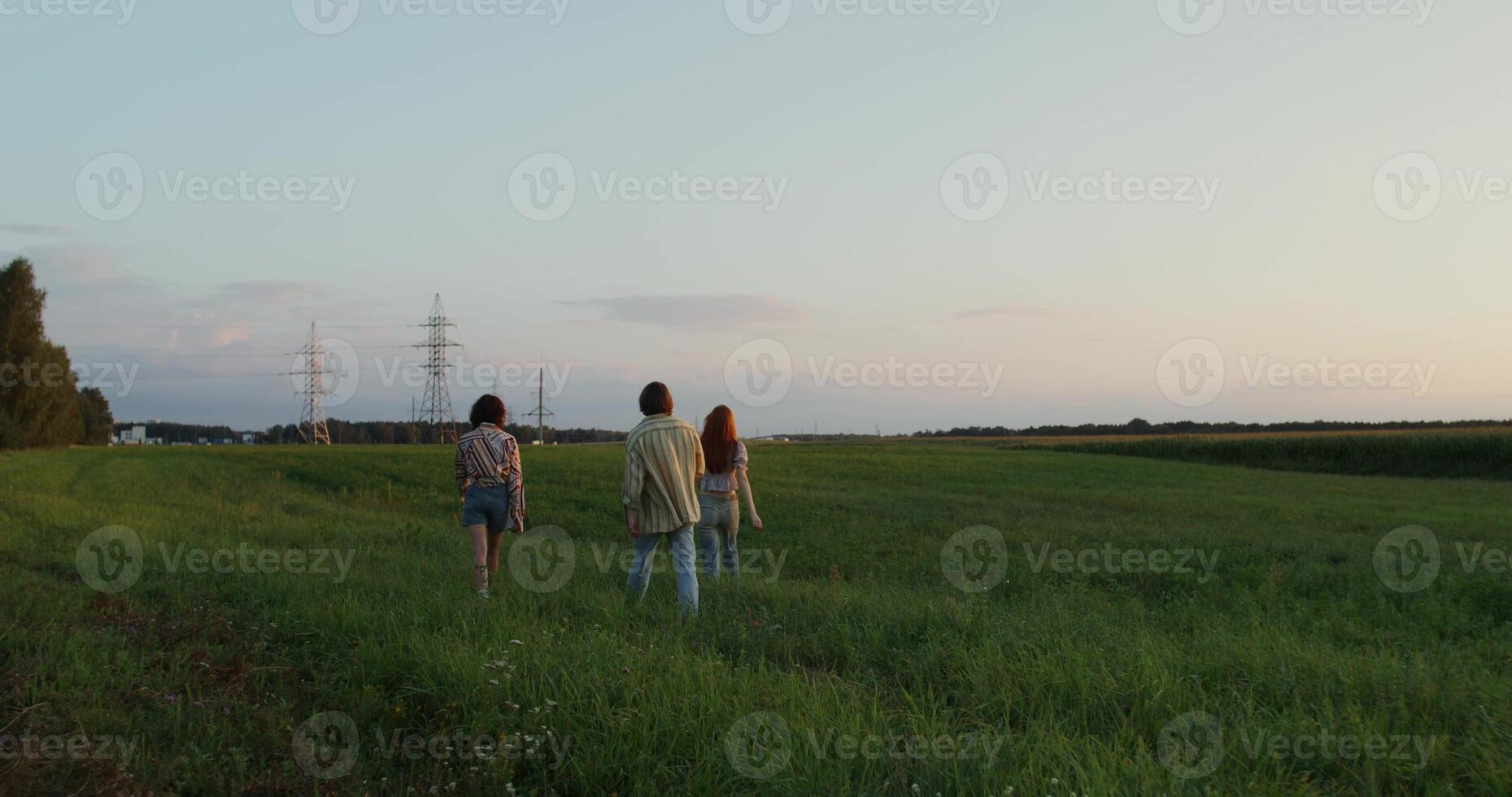 Three young people are talking and smiling while walking in a field photo