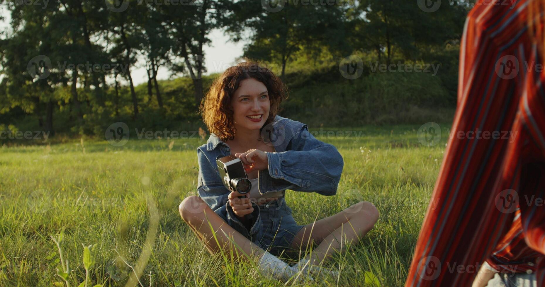 Two young women are photographed with a camera in the tall grass in a field. photo