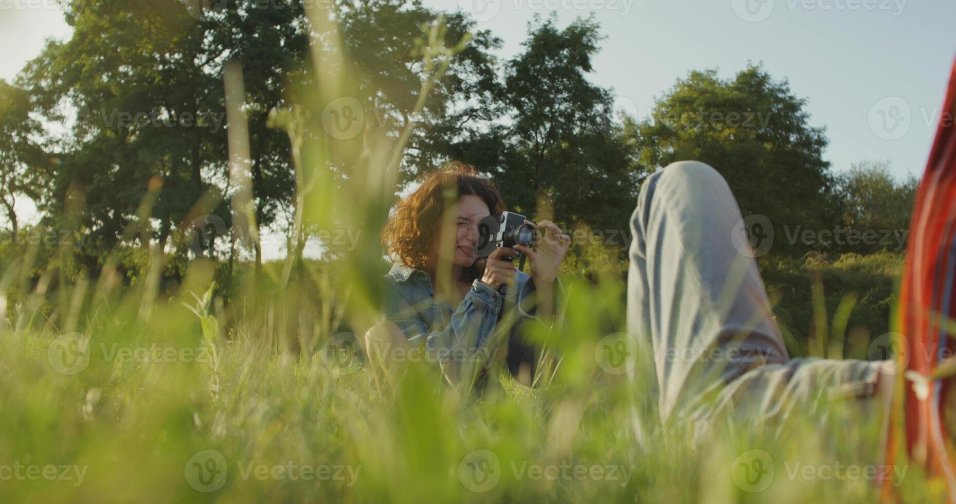 Two young women are photographed with a camera in the tall grass in a field. A sunny summer day photo