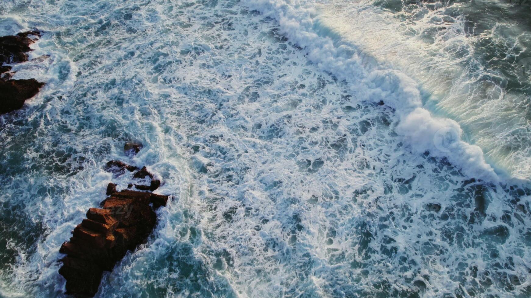 Top view of the foaming sea waves washing the coastal rocks, drone - foaming photo