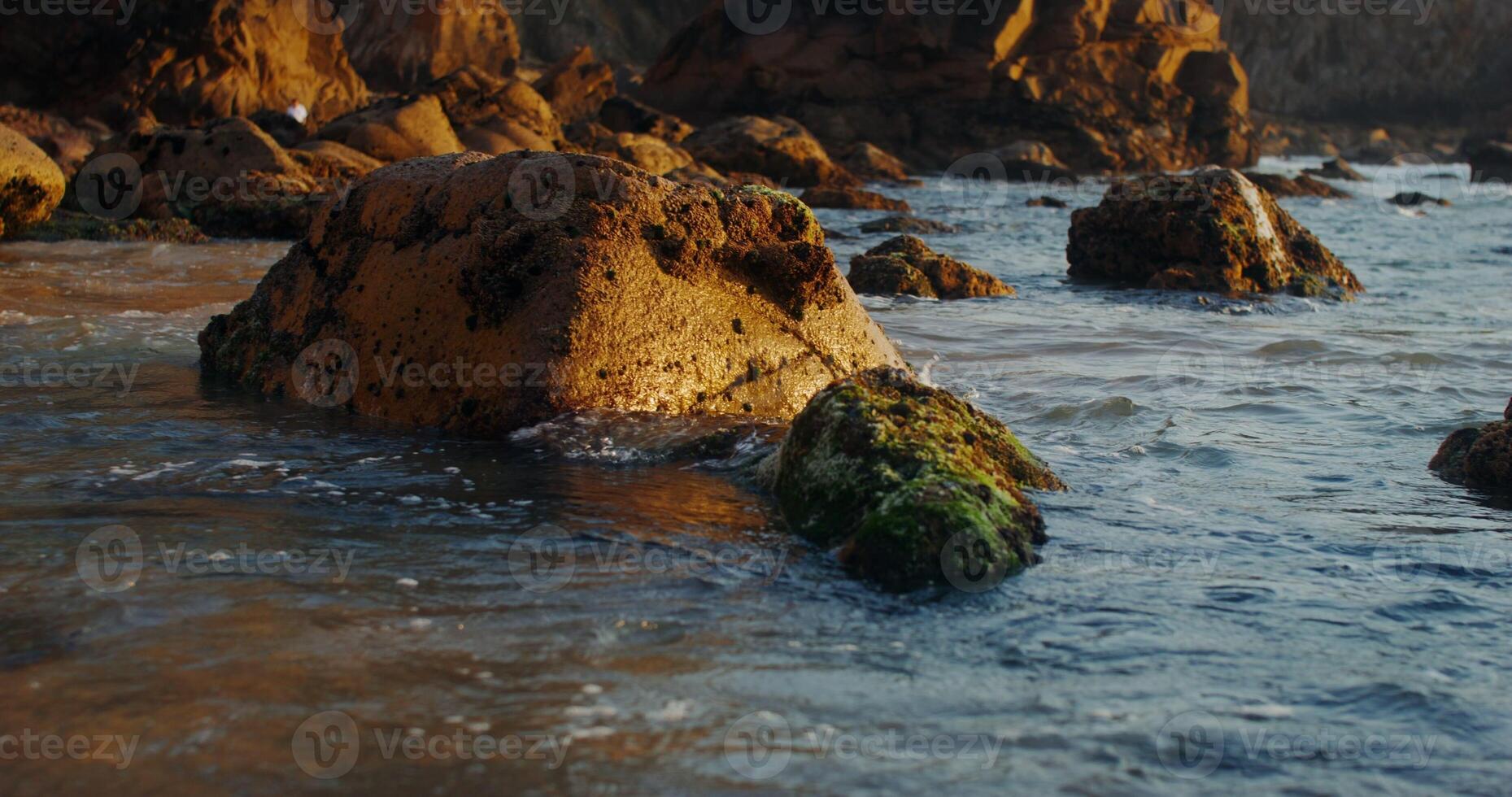 Foamy sea waves crash against the rocks on the shore at sunset photo