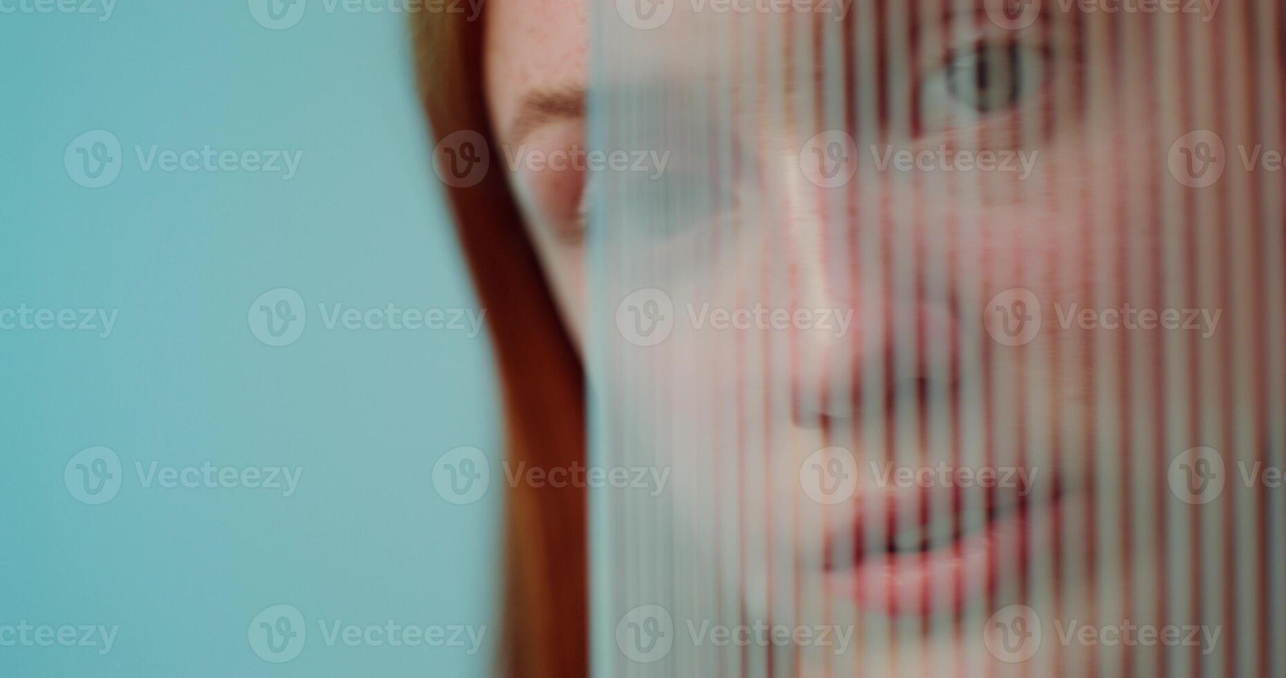 A red-haired woman with freckles is smiling at the camera while standing on a studio background. She hides behind plexiglass photo
