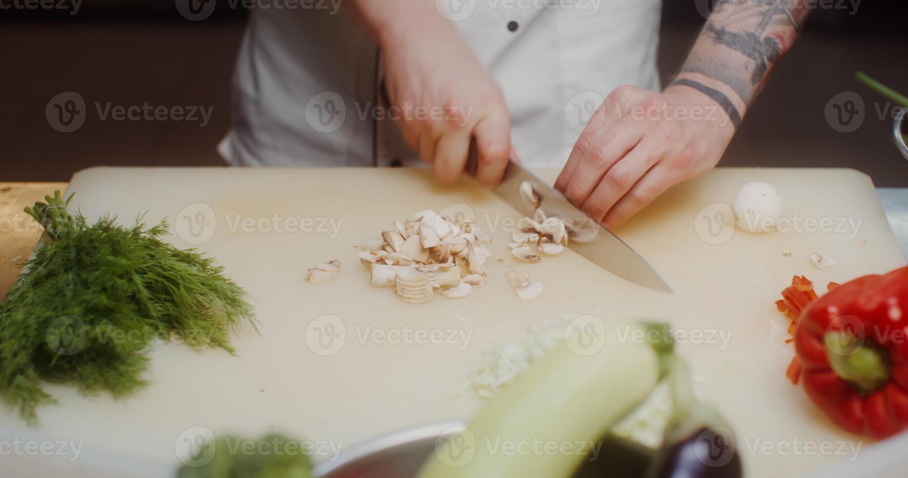 A man in a chef's uniform cuts mushrooms and then puts them in a frying pan standing on the stove, close-up of his hands photo