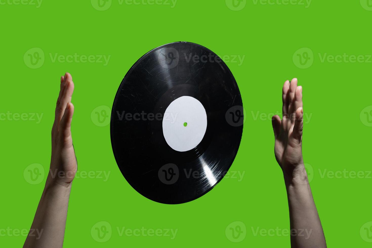 A vinyl record elegantly floating between two hands against a vibrant green background photo