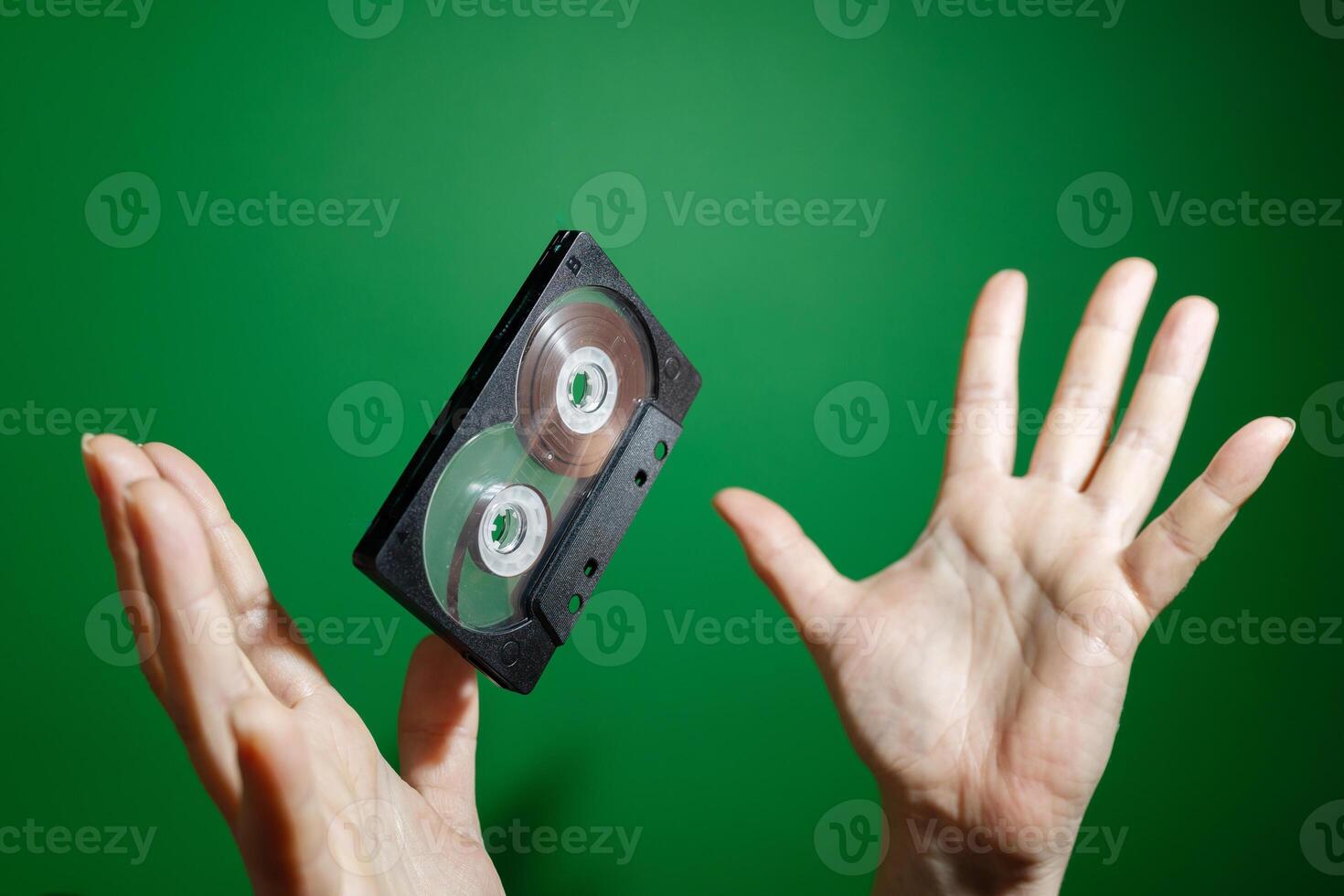 A Flying VHS Tape is Held in Hands Against a Vibrant Green Background in Artistic Style photo